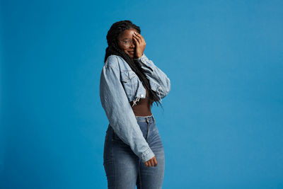 Young woman looking away while standing against blue wall