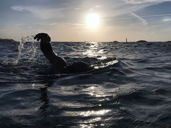 Silhouette person swimming in sea against sky during sunset