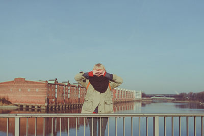 Portrait of smiling young woman standing on railing against clear sky