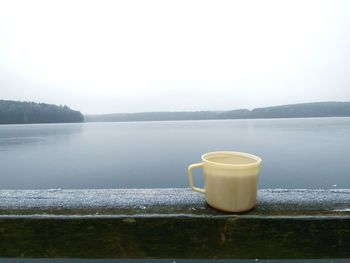 Close-up of coffee cup by lake against clear sky