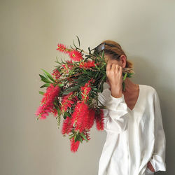 Portrait of  woman standing against wall holding bouquet of bottlebrush flowers 