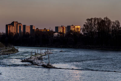 Frozen river by buildings against sky at dusk