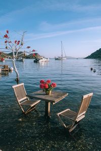 Empty chairs and tables and lounge chair by sea against sky