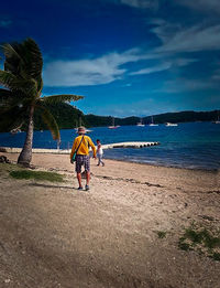 Rear view of men walking on beach against sky