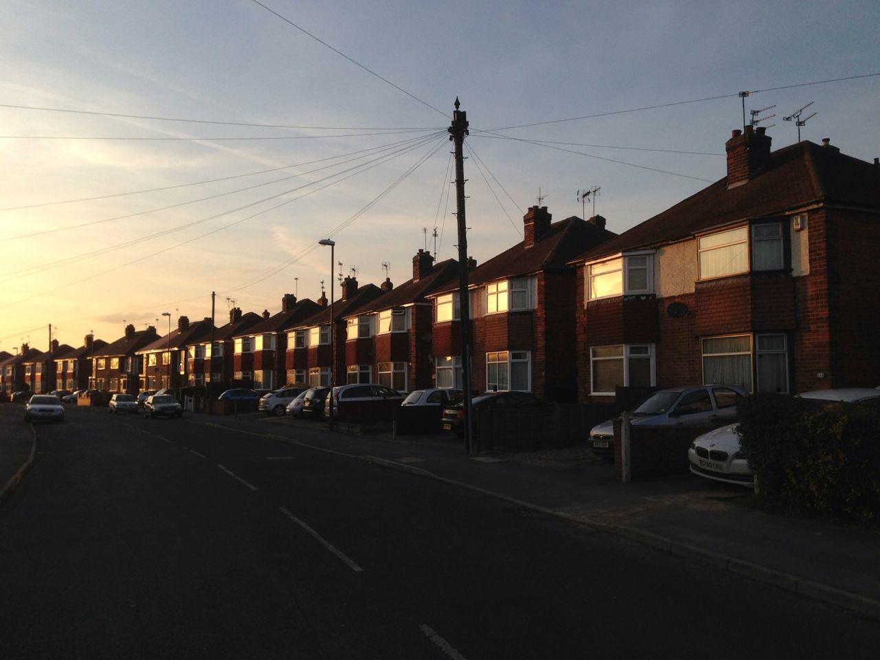 building exterior, architecture, built structure, transportation, power line, sky, street, cable, electricity pylon, mode of transport, city, road, car, land vehicle, residential structure, the way forward, cloud, electricity, sunset, residential building