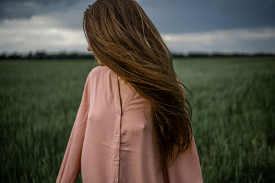 Young girl with long hair on green field in windy weather.