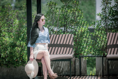 Beautiful woman sitting on bench against trees