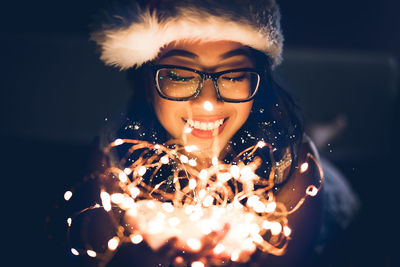 Portrait of smiling young woman holding lit candles in the dark