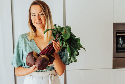 Young european woman holding beetroot while smiling at camera