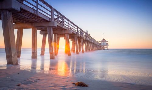 Pier over sea against clear sky during sunset