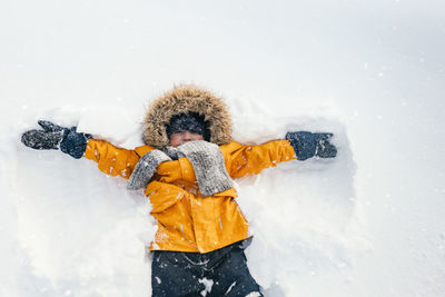 Happy boy is a child playing on a winter walk in nature. a child makes a snow angel.