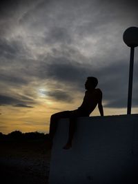 Silhouette man standing on rock against sky during sunset