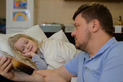 Dad entertains the child during illness, he looks, reads a book, a photo book with his daughter home