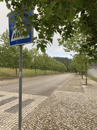 Road sign by trees on footpath in city