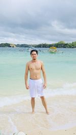 Young man standing at beach against sky