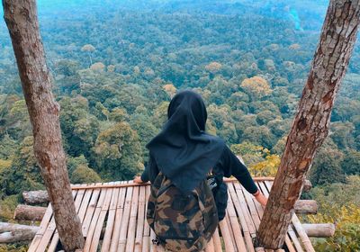 Rear view of woman sitting on wooden platform against forest