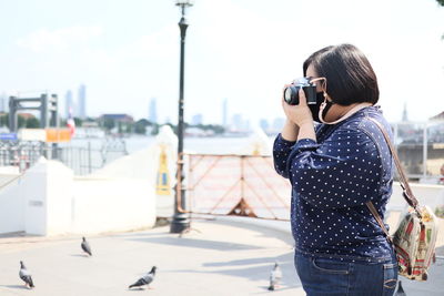 Woman wearing mask with camera standing at harbor