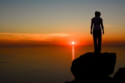 Rear view of silhouette man standing against sea during sunset