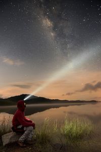 Man sitting by lake against sky at night