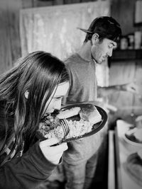 Girl eating food while standing with man in kitchen