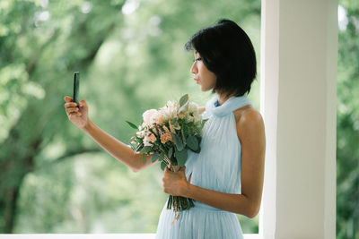 Beautiful young woman taking selfie while holding flower bouquet