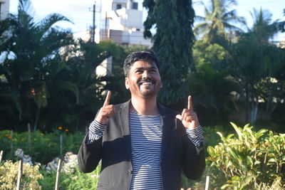 Smiling young man pointing up while standing in public park