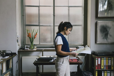 Businesswoman analyzing blueprint while standing at home office