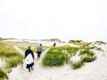 Rear view of friends carrying surfboards while walking at beach against clear sky