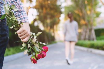 Midsection of man holding flowers while standing by woman on footpath