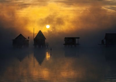 Silhouette houses by sea against sky during sunset