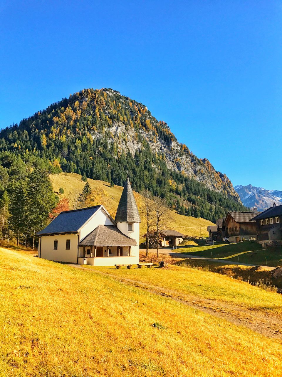 built structure, architecture, house, building exterior, mountain, country house, grass, tranquil scene, landscape, tranquility, no people, scenics, field, day, blue, nature, tree, outdoors, barn, clear sky, beauty in nature, sky, farmhouse