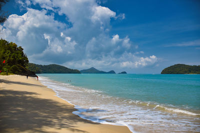 Waves of the azure andaman sea under the blue sky reaching the shores of cenang beach in langkawi