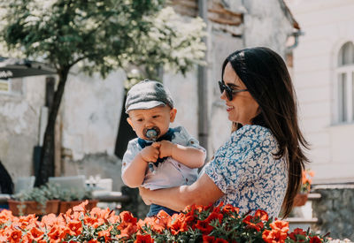 Mother holding her baby while watching flowers in city