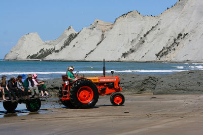 People sitting in tractor at beach against sky