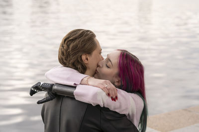 Woman with amputated hand kissing boyfriend on cheek by river