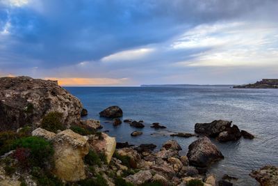 Scenic view of sea and rocks against cloudy sky