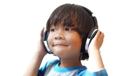 Close-up of boy looking away while listening music against white background