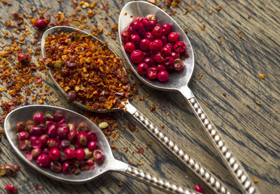 Close-up of chili flakes and dried fruits in spoons on wooden cutting board