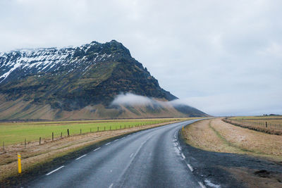 Country road by mountains against sky