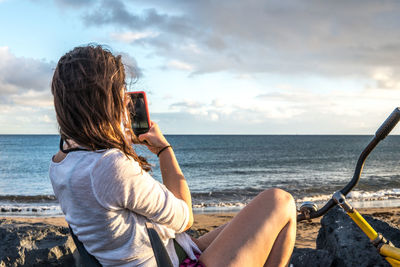 Rear view of woman photographing sea against sky