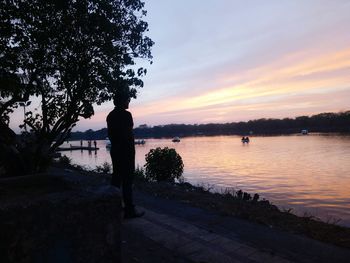 Silhouette man by tree against sea during sunset