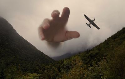 Digital composite image of hand reaching towards airplane in foggy weather