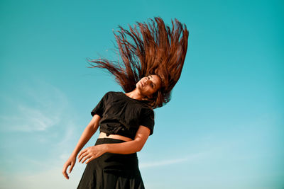 Low angle view of woman flipping hair standing against sky