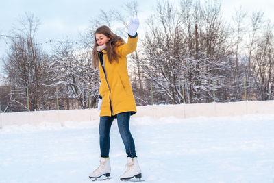 Portrait of happy young woman in yellow jacket skating at the rink