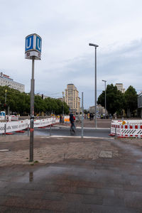 Road sign by street against sky in city