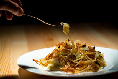 Cropped image of hand holding noodles in plate on table