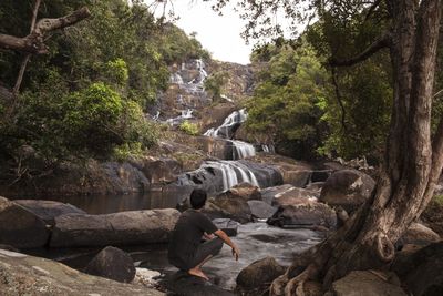 Full length of man crouching on rock at temburun waterfall in tarempa