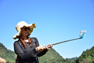 Woman taking selfie with smart phone against clear blue sky