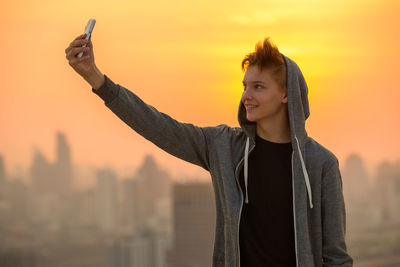 Young man using smart phone against sky during sunset