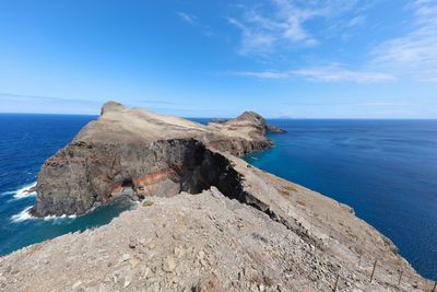 Scenic view of rocky shore by sea against blue sky